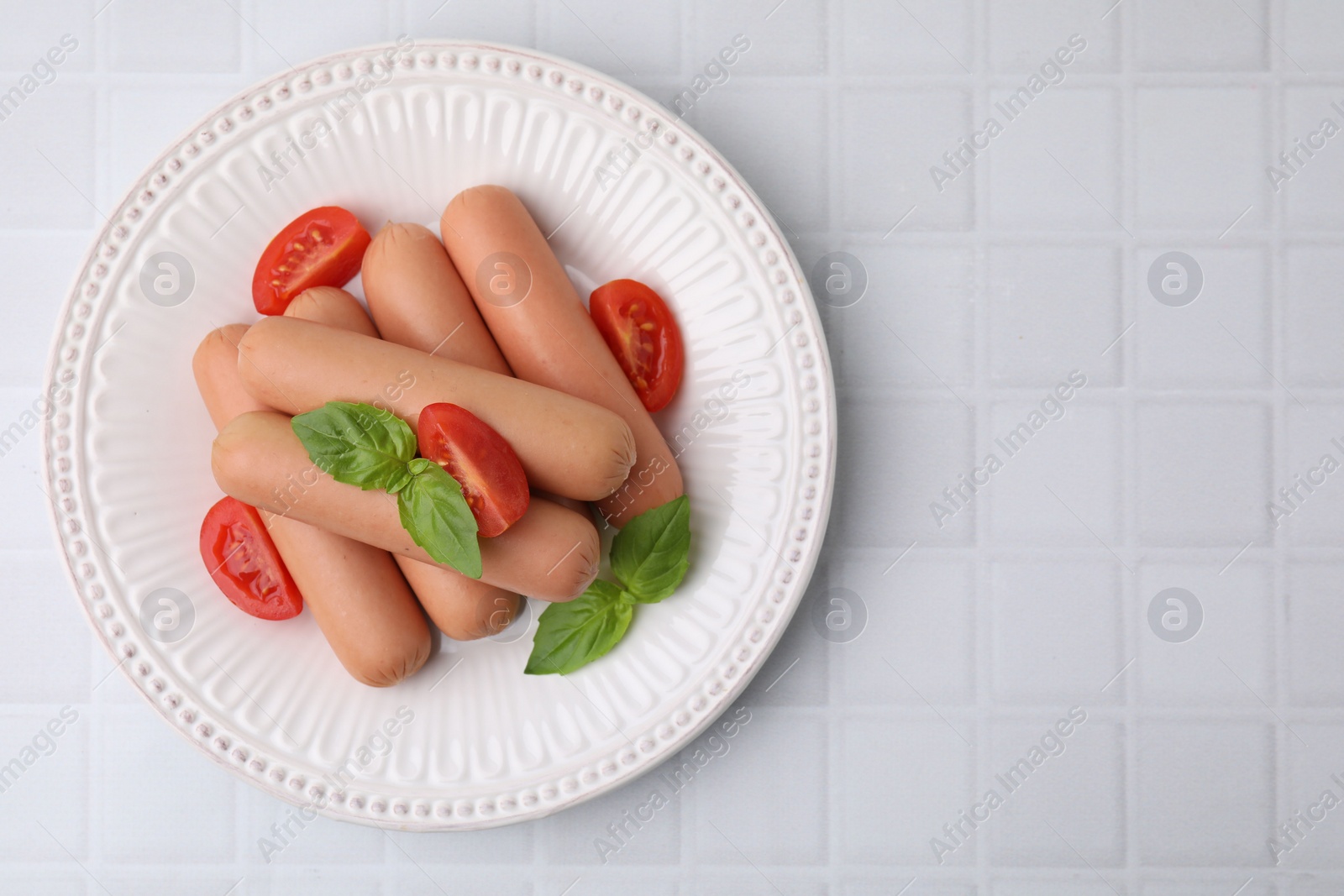 Photo of Delicious boiled sausages, tomatoes and basil on white tiled table, top view. Space for text