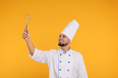 Photo of Happy professional confectioner in uniform holding whisk on yellow background