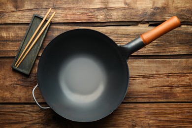 Photo of Empty iron wok and chopsticks on wooden table, flat lay
