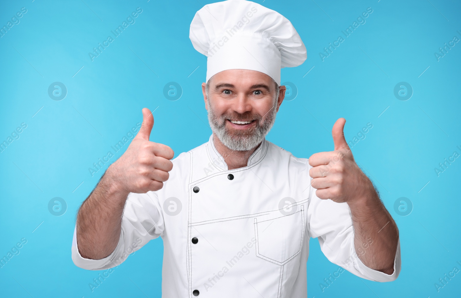 Photo of Happy chef in uniform showing thumbs up on light blue background