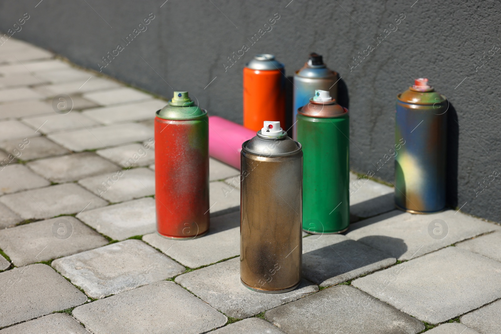 Photo of Cans of different spray paints on pavement near wall