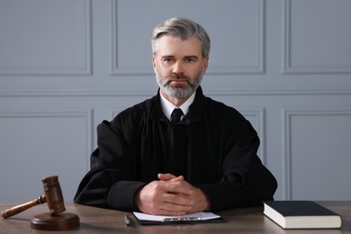 Photo of Judge with gavel, papers and book sitting at wooden table indoors