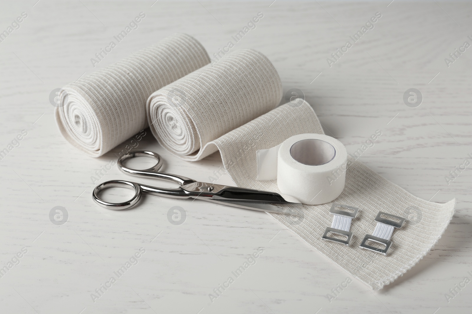 Photo of Medical bandage rolls, sticking plaster and scissors on white wooden table