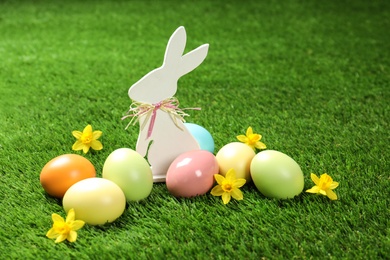 Photo of Cute wooden Easter bunny and dyed eggs on green grass