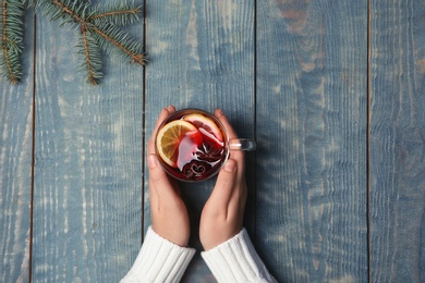 Photo of Woman holding cup with hot mulled wine on table, top view