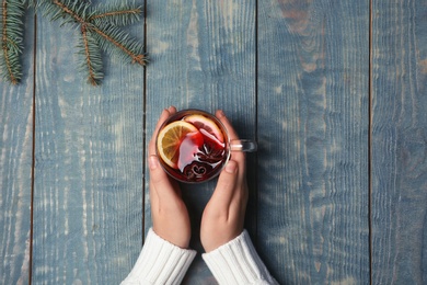 Woman holding cup with hot mulled wine on table, top view