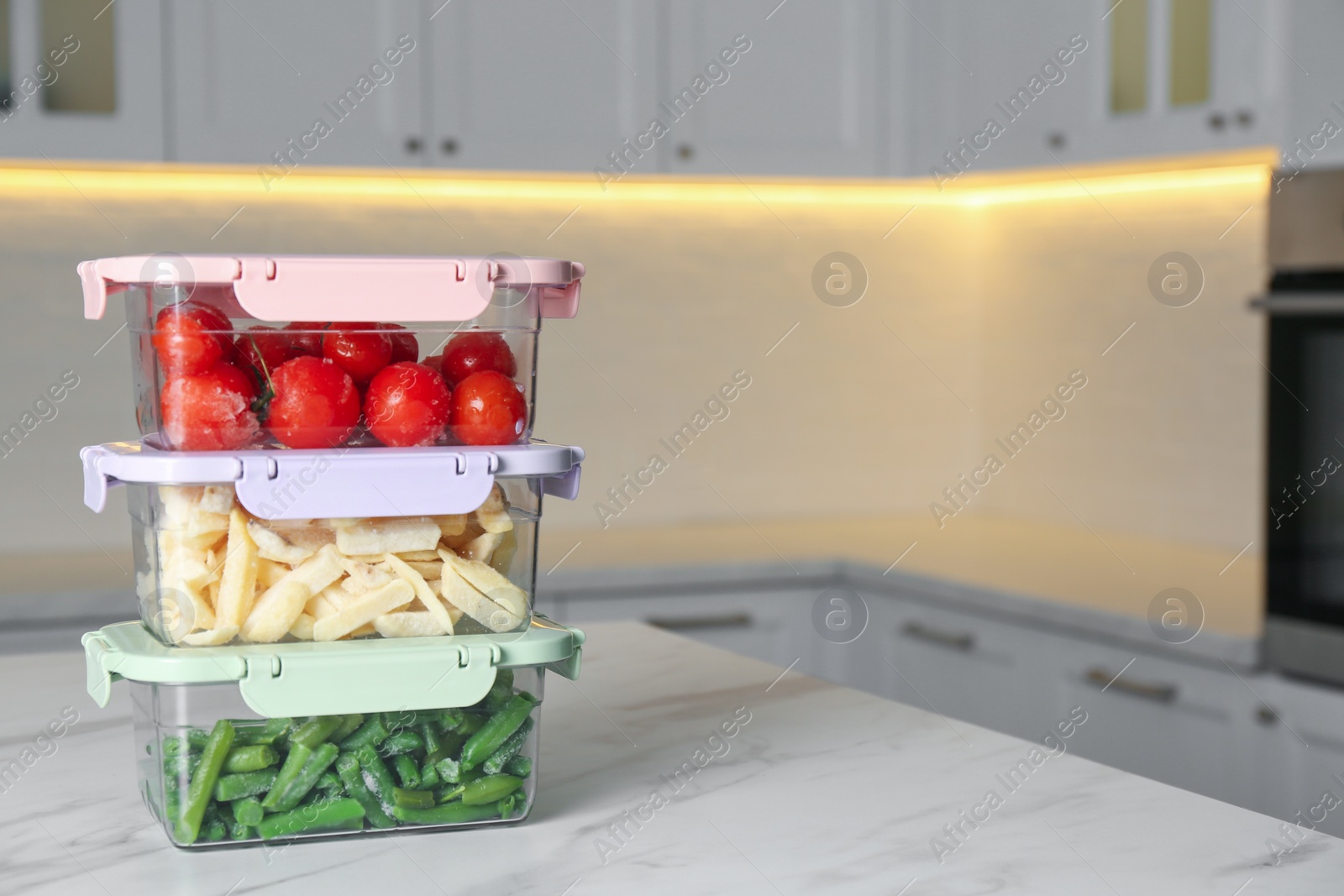 Photo of Containers with different frozen vegetables on white marble table in kitchen. Space for text