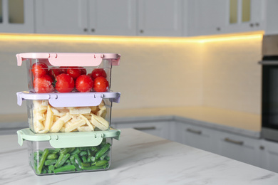 Photo of Containers with different frozen vegetables on white marble table in kitchen. Space for text