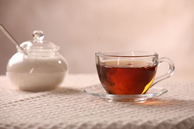 Aromatic tea in cup, saucer and sugar on table