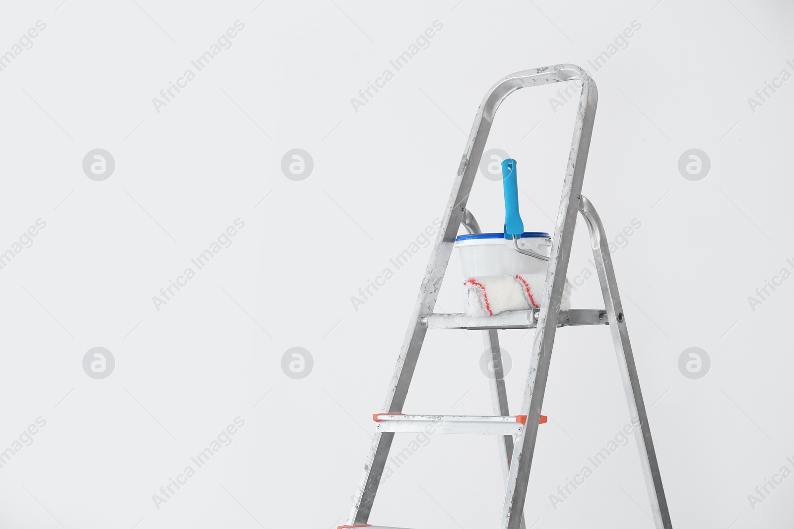 Photo of Bucket with paint and roller on step ladder near white wall