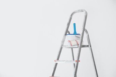 Photo of Bucket with paint and roller on step ladder near white wall