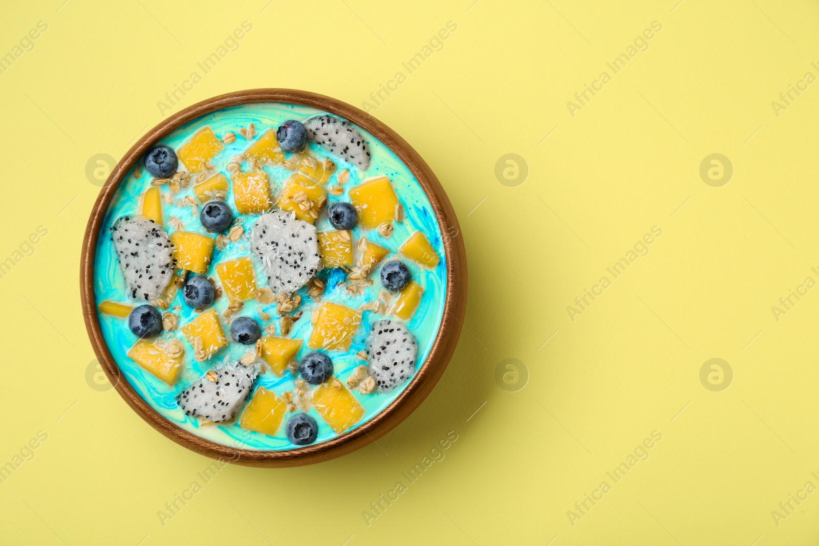 Photo of Delicious smoothie bowl with fresh fruits, blueberries and oatmeal on yellow background, top view. Space for text