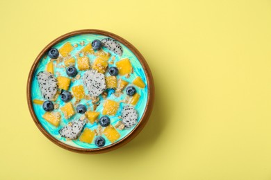 Delicious smoothie bowl with fresh fruits, blueberries and oatmeal on yellow background, top view. Space for text