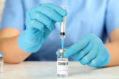 Doctor filling syringe with coronavirus vaccine at table in laboratory, closeup