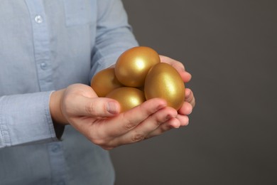 Photo of Woman holding shiny golden eggs on grey background, closeup