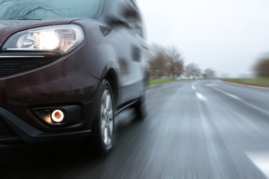 Image of Car driving at high speed on rainy day outdoors, closeup with motion blur effect. Space for text