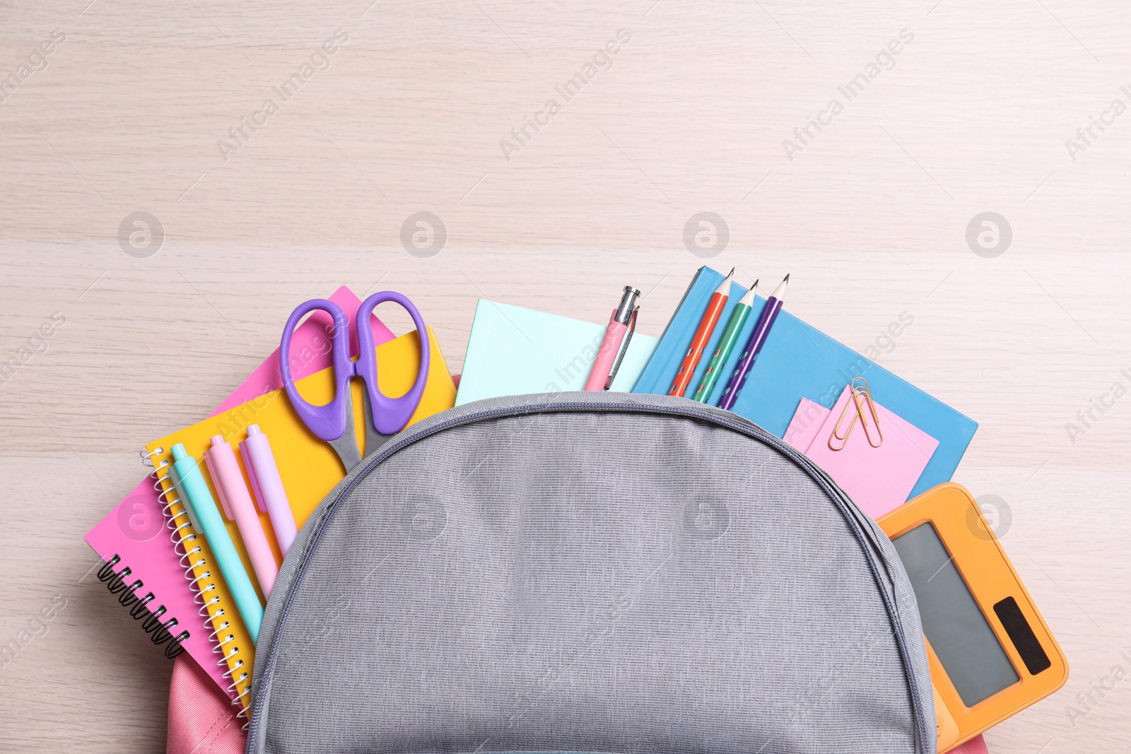 Photo of Backpack with different school stationery on wooden table, top view