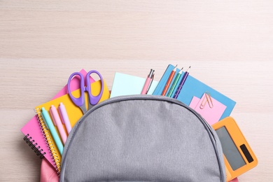Photo of Backpack with different school stationery on wooden table, top view