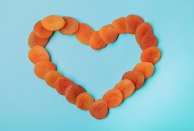 Photo of Heart shaped frame made of dried apricots on color background, top view with space for text. Healthy fruit