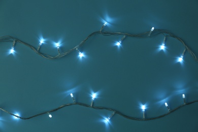 Glowing Christmas lights on turquoise background, flat lay