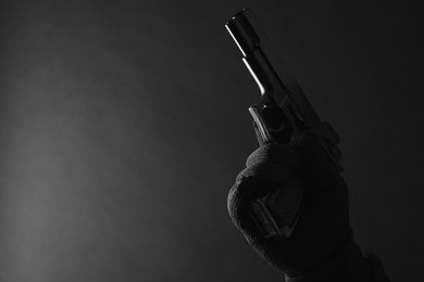 Armed robbery. Dangerous criminal with gun on black background, closeup. Space for text