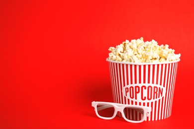 Photo of Bucket of fresh tasty popcorn and glasses on color background, space for text. Cinema snack