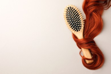 Photo of Wooden brush and red hair strand on light background, top view. Space for text