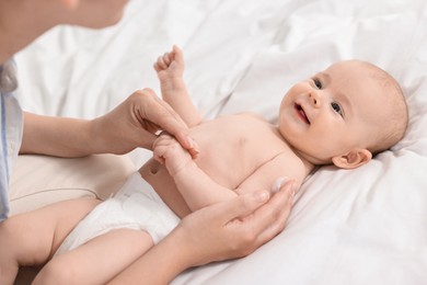 Photo of Woman applying body cream onto baby`s skin on bed, closeup