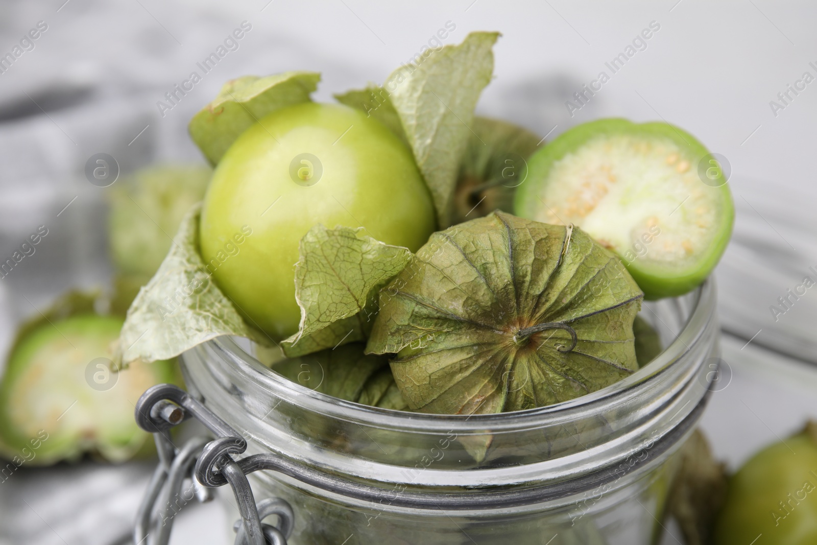 Photo of Fresh green tomatillos with husk in glass jar on table, closeup