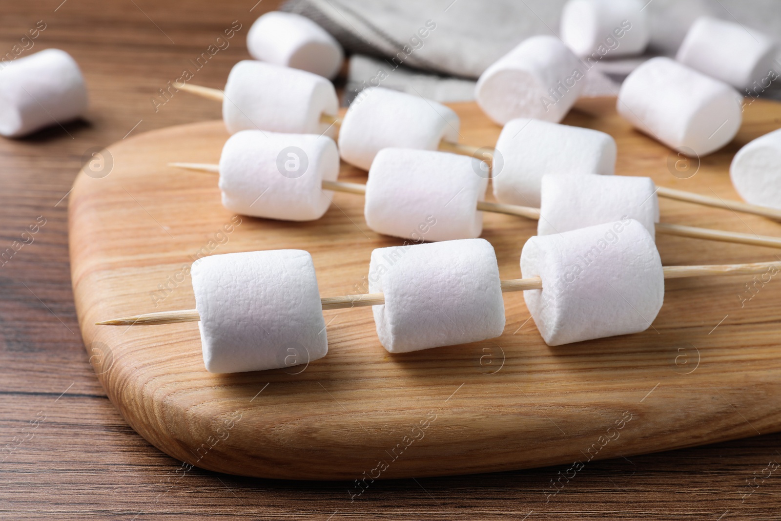 Photo of Sticks with delicious puffy marshmallows on wooden table, closeup