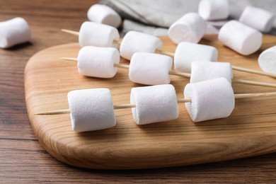 Photo of Sticks with delicious puffy marshmallows on wooden table, closeup