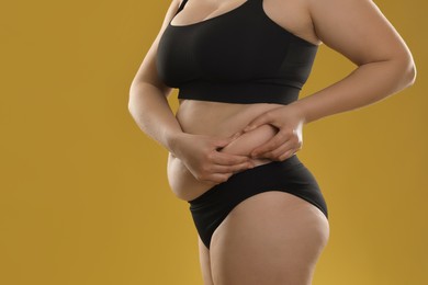 Photo of Woman touching belly fat on goldenrod background, closeup. Overweight problem