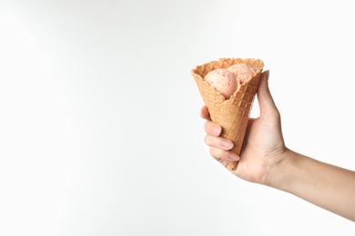 Woman holding delicious ice cream in waffle cone on white background, closeup