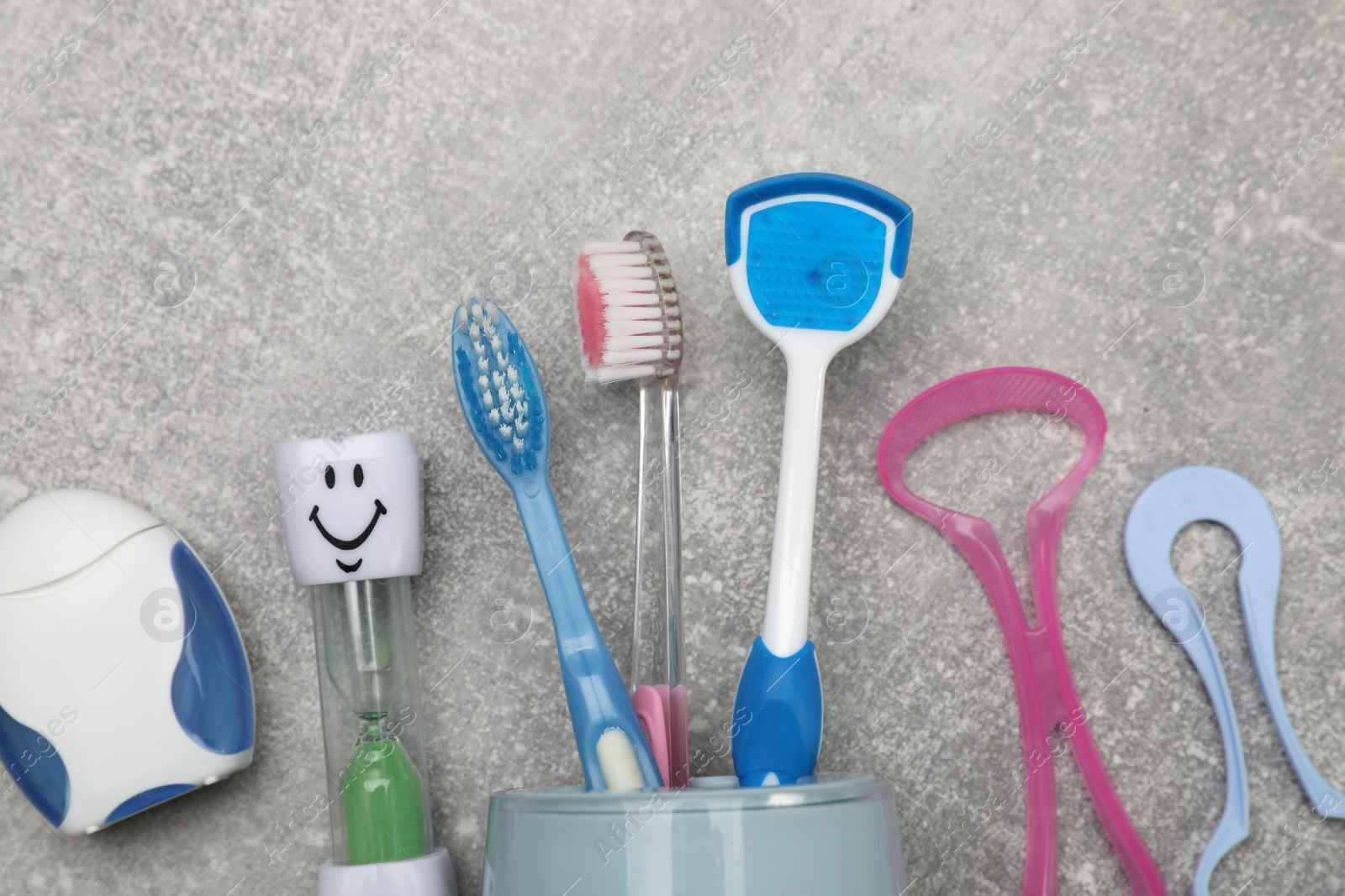 Photo of Tongue cleaners, toothbrushes, dental floss and hourglass on light grey background, flat lay