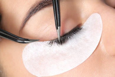 Young woman undergoing eyelashes extensions procedure, closeup