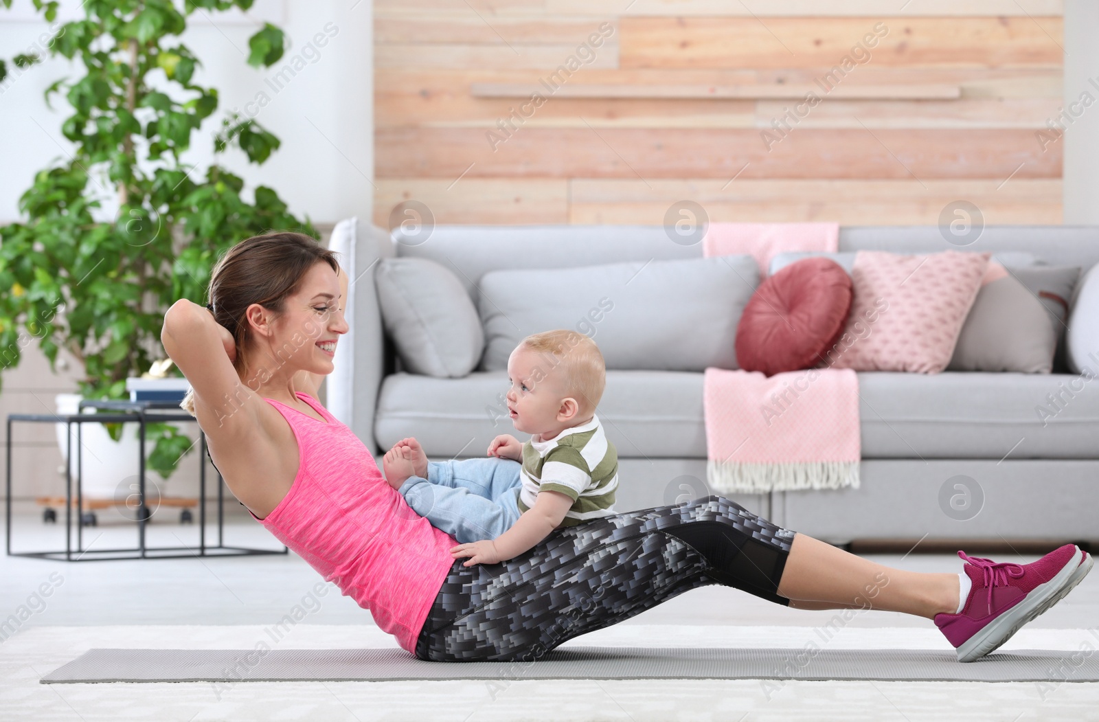 Photo of Young sportive woman doing exercise with her son at home. Fitness training