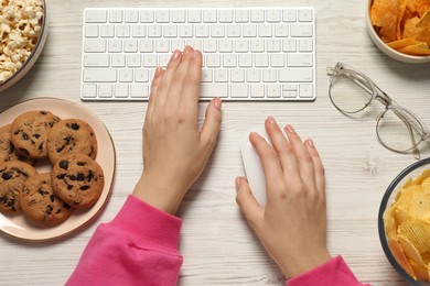 Photo of Bad eating habits. Woman working on computer at white wooden table with different snacks, top view