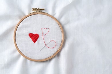 Photo of Embroidered red hearts and needle on white cloth, top view. Space for text