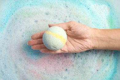 Woman holding color bath bomb over foam, top view