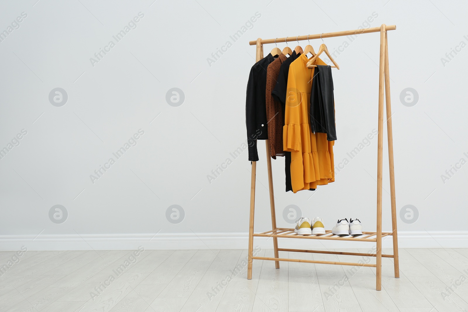 Photo of Wooden rack with stylish clothes in room. Space for text