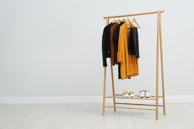 Photo of Wooden rack with stylish clothes in room. Space for text