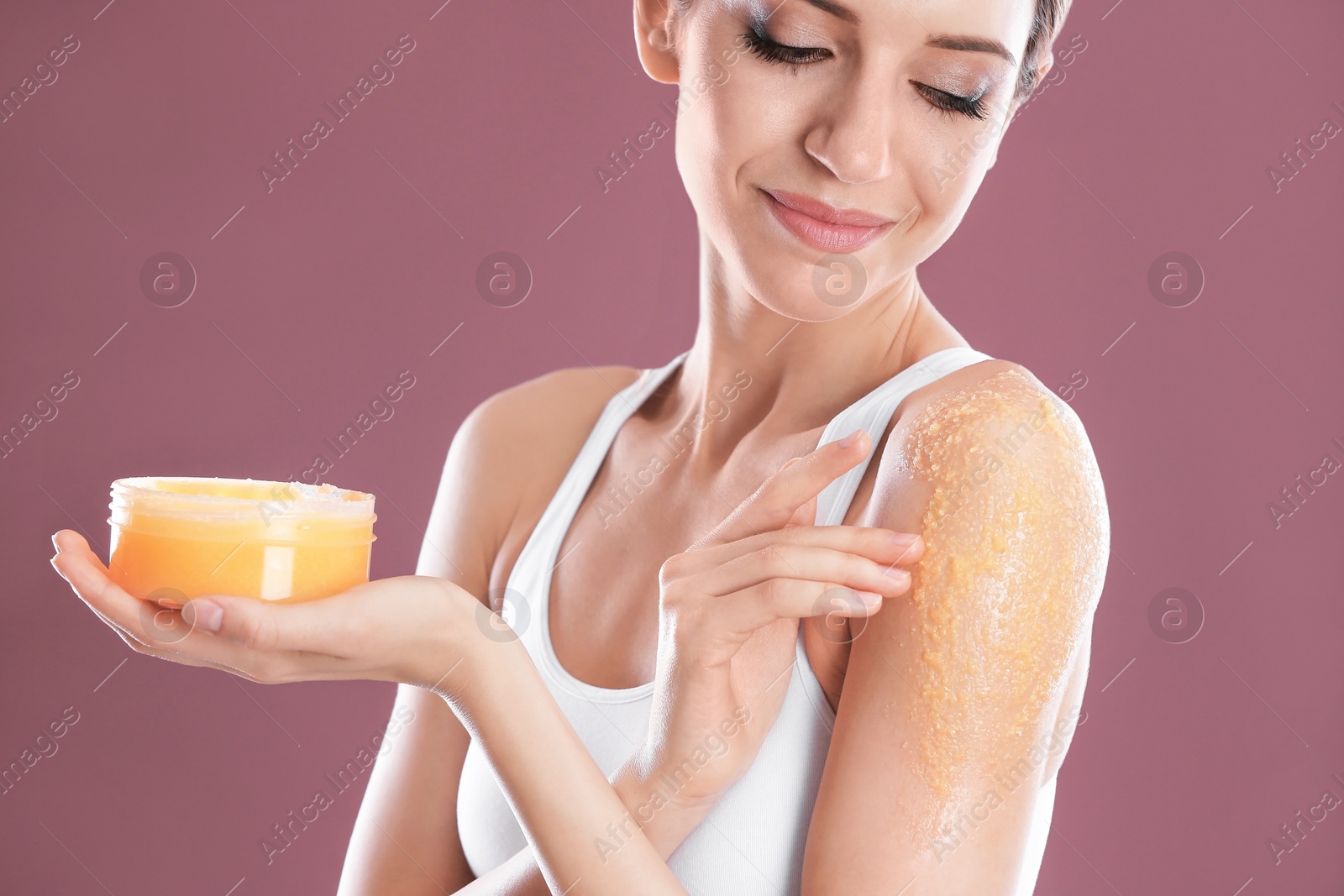 Photo of Young woman applying natural scrub on her shoulder against color background