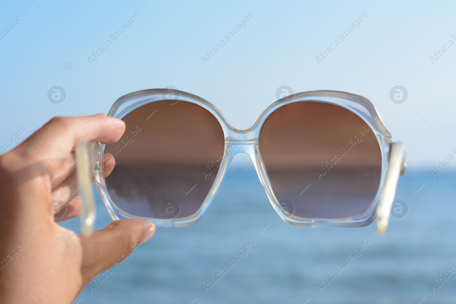 Photo of Woman holding stylish sunglasses near sea, closeup