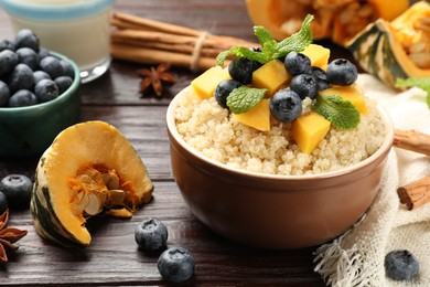 Photo of Tasty quinoa porridge with blueberries, pumpkin and mint in bowl on wooden table