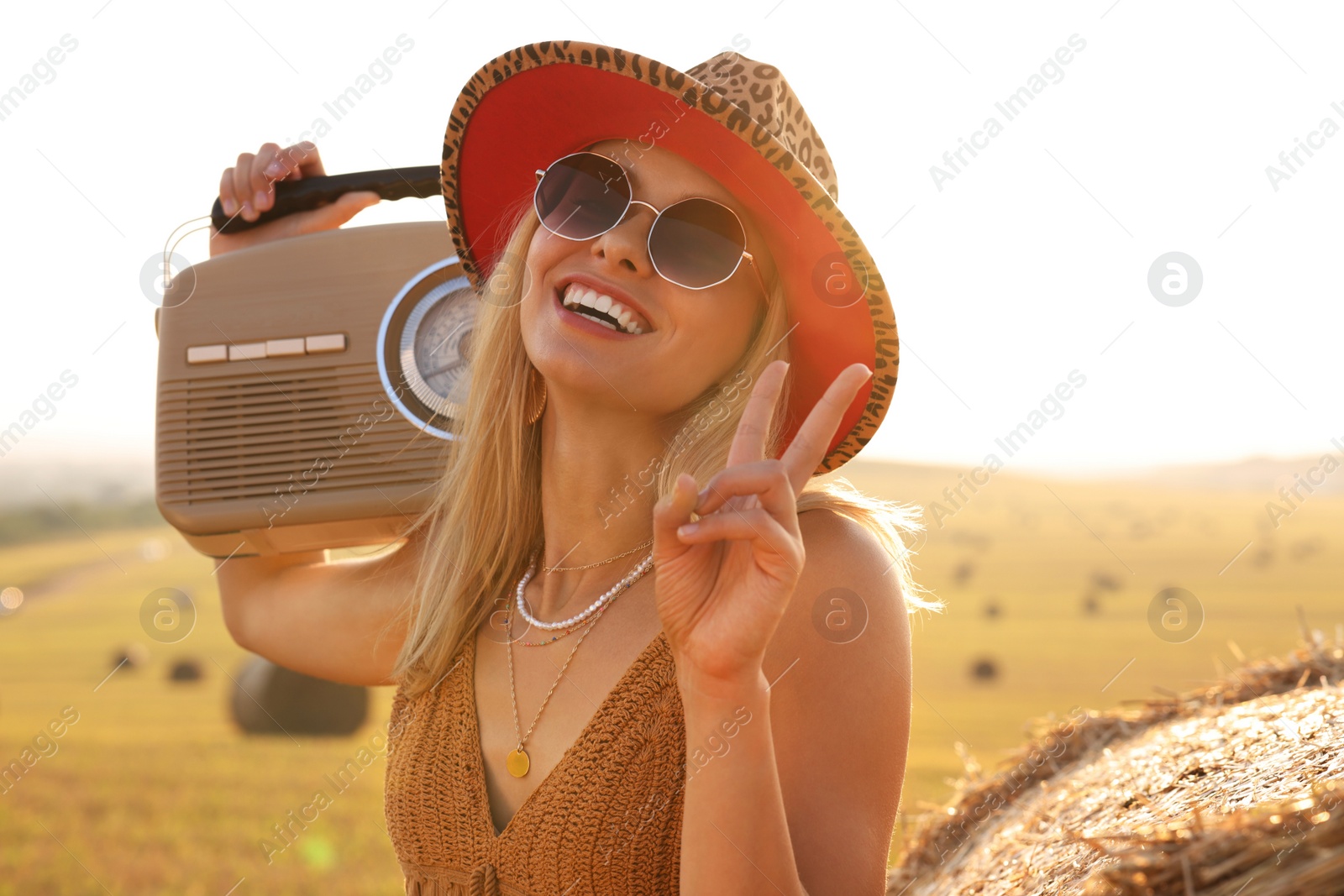 Photo of Happy hippie woman with radio receiver showing peace sign in field