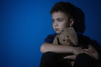 Photo of Sad little boy with toy near blue wall, space for text. Domestic violence concept