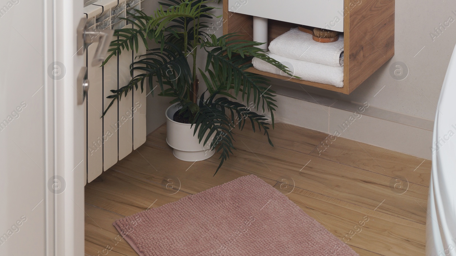 Photo of Soft bath mat near houseplant on wooden floor in bathroom