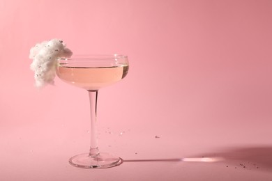 Tasty cocktail in glass decorated with cotton candy on pink background, space for text