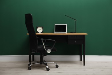 Stylish workplace with laptop and comfortable armchair near green wall indoors. Interior design