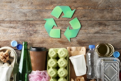 Photo of Recycling symbol and different garbage on wooden background, top view